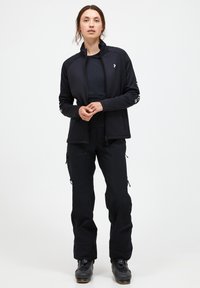 Giacca nera con zip e colletto alto, pantaloni neri abbinati e stivali da neve neri. Presenta tasche con zip e un design aderente.
