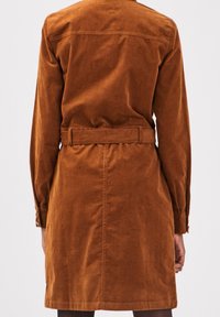 Hnědá kordurová šaty s dlouhými rukávy, pásem v pase a délky po kolena. Má jednoduchý design zadní části a manžety na knoflíky.