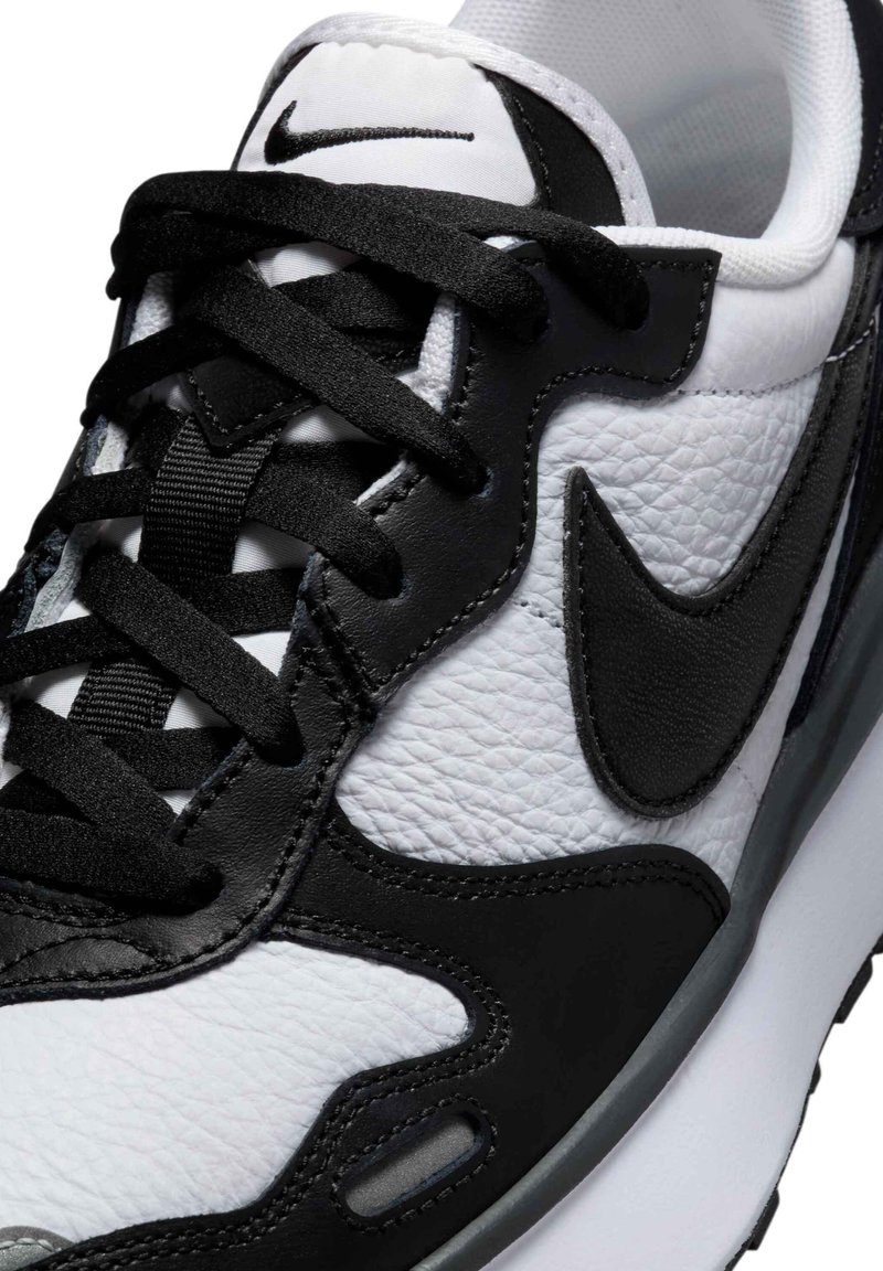 Zapatillas Nike en blanco y negro que presentan un upper de cuero texturizado, acentos suaves, cordones negros y un diseño de swoosh en contraste.