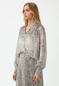 Luipaardprint blouse van lichtgewicht, doorzichtig materiaal met een kraag en lange, geplooide mouwen, gecombineerd met een bijpassende rok.