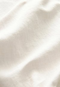 Tissu en lin blanc doux avec une texture naturelle et des plis délicats, mettant en valeur ses qualités respirantes et légères.