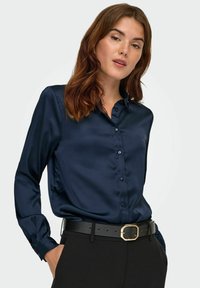 Navy satijnen blouse met lange mouwen en een knoopsluiting aan de voorkant. Kenmerkt zich door een klassieke kraag en een gladde, glanzende textuur. Zwarte riem met een gouden gesp.