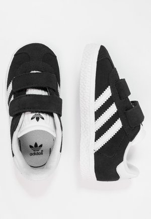 Schwarze Adidas-Sneaker mit weißen Streifen, Klettverschlüssen und strukturierten weißen Sohlen, von oben und von der Seite auf weißem Hintergrund gezeigt.