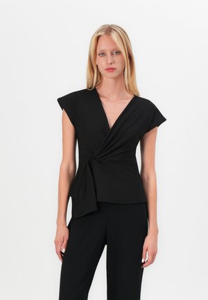 Black wrap-style top with short cap sleeves, featuring a twisted front detail and a smooth texture. Worn with matching black trousers.
