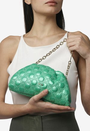 Borsa a tracolla verde trapuntata realizzata in materiale lucido, con una tracolla a catena e un motivo floreale. La borsa è tenuta in mano da una persona.