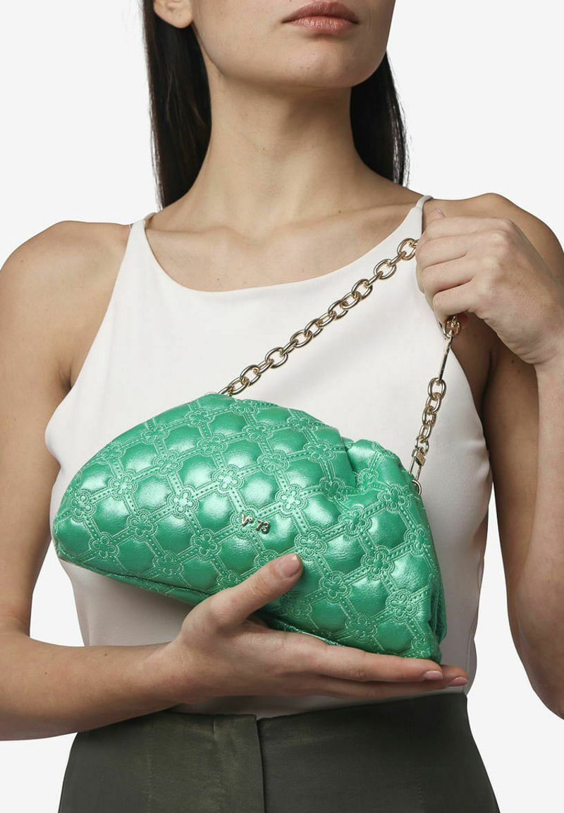 Borsa a tracolla verde trapuntata realizzata in materiale lucido, con una tracolla a catena e un motivo floreale. La borsa è tenuta in mano da una persona.