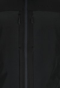 Zwarte zip-up jas met een gladde textuur, twee voorritsen met trekstangen en een logo aan de bovenste linkerkant.