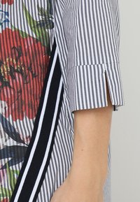 Koszula w paski z kwiatowym wzorem, z krótkimi rękawami, czarno-białymi paskowanymi akcentami oraz bocznym rozcięciem. Materiał bawełniany.