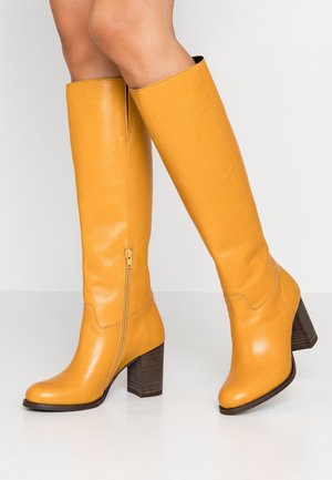Żółte skórzane kozaki do kolan z bocznym zamkiem błyskawicznym, masywnym drewnianym obcasem i gładką fakturą. Okrągły nosek i bezszwowy design.