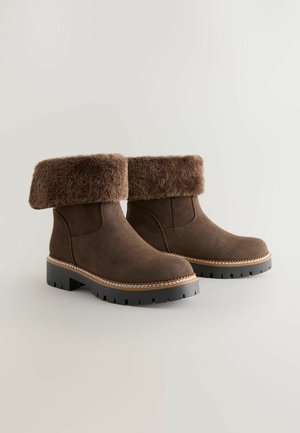 Brown suede ankle boots with a fuzzy, foldable cuff and a thick black rubber sole, featuring a stitched detail around the sole edge.