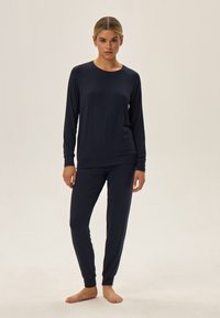 Granatowy zestaw odzieży domowej wykonany z miękkiego materiału; bluza z długim rękawem i okrągłym dekoltem oraz dopasowane spodnie z elastycznymi mankietami. Gładka tekstura na całej powierzchni.