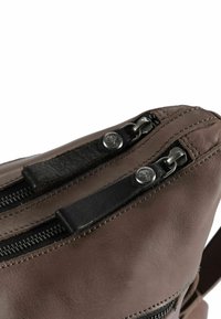 Bruine leren tas met twee ritssluitingen, voorzien van zwarte leren accenten en zilverkleurige hardware. Gladde textuur met zichtbare stikdetails.