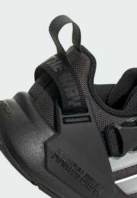 Chaussure de sport noire avec un upper en tissu texturé, une semelle en caoutchouc et un accent en plastique prononcé portant l'inscription "MANDALORIAN".