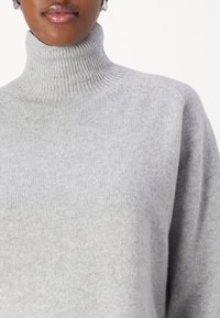 Grauer Rollkragenpullover aus weichem Strickmaterial, mit geripptem Kragen und nahtlosen Schultern. Die Oberfläche wirkt glatt und gemütlich.