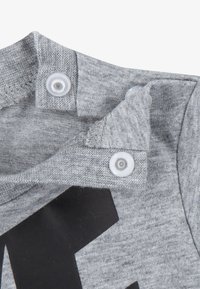 Šedá košile s krátkým rukávem, která má černou grafiku písmen, je vyrobena z měkkého materiálu a má patentky na límci pro snadné oblékání.