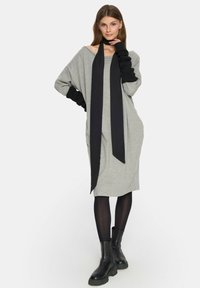 Szara oversized sukienka z czarnym detalem w postaci chusty. Długie rękawy z prążkowanymi mankietami. Noszona z czarnymi botkami za kostkę i czarnymi rajstopami.