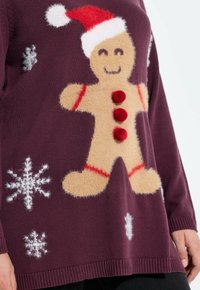 Jersey burdeos con un diseño de hombre de jengibre esponjoso en color beige, botones rojos y patrones de copos de nieve en blanco en la parte delantera. Los detalles incluyen un sombrero rojo.