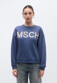 Μπλε φούτερ με στρογγυλή λαιμόκοψη, υπερμεγέθη εφαρμογή και κρέμ γράμματα "MSCH" μπροστά. Υλικό από βαμβακερό μείγμα, με ριμπ μανσέτες και τελείωμα.