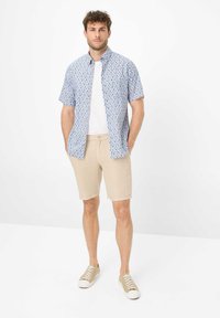 Blauwe gestreepte korte mouwen overhemd over een wit T-shirt, gecombineerd met beige shorts en beige sneakers, alles in een casual pasvorm.