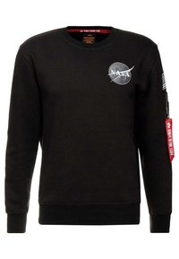 Svart crewneck sweatshirt med vit NASA-logotyp på bröstet, amerikansk flagga-patch på ärmen och röd "Remove Before Flight" dragkedjetag på ärmfickan.
