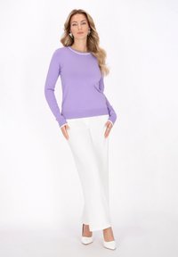 Helllila langärmliger Strickpullover mit einem weißen gestreiften Ausschnitt, kombiniert mit weißen weit geschnittenen Hosen und weißen High Heels.
