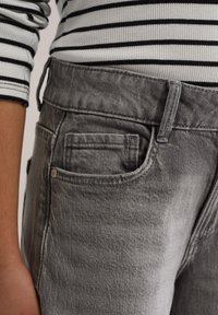 Hallid teksapüksid tekstuurse viimistlusega, küljetasku, vööaasade ja õrna tuhmumise efektiga. Üleval kihina triibuline pikkade varrukatega särk.