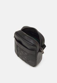 Borsa a tracolla nera in pelle con fronte texturizzato, chiusura con zip e interno verde a contrasto. Presenta dettagli logo e tracolla regolabile.