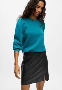 Teal pullover sweater med puffede ærmer, parret med en sort faux læderskirt med en sideslids. Glat tekstur og tætsiddende design.