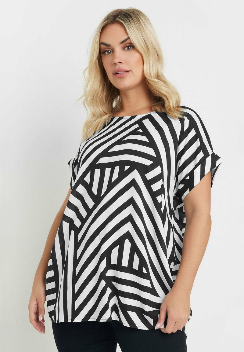 Haut noir et blanc avec un motif rayé géométrique, présentant une coupe ample, un col rond et des manches courtes. Texture lisse.