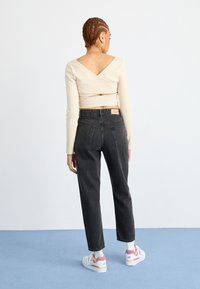 Béžový dlhý rukáv top s prekrytím, skombinovaný s čiernymi džínsy so zvýšeným pásom. Tenisky sú biele s ružovými akcentmi. Minimalistický dizajn, jemná textúra.