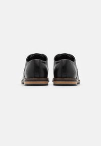 Chaussures en cuir noir avec une texture lisse, talon bas et accents en bois brun clair. Talon arrondi et design minimaliste.