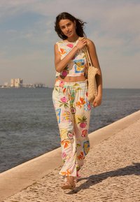 Bloemmotief crop top en bijpassende broek, met levendige fruitontwerpen. Een gehaakte tas en sandalen complementeren de lichte, zomerse outfit.