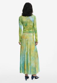 Maglietta a maniche lunghe aderente e gonna fluida plissè con un motivo tie-dye nei toni di verde, blu e arancione; tessuto morbido e leggero.