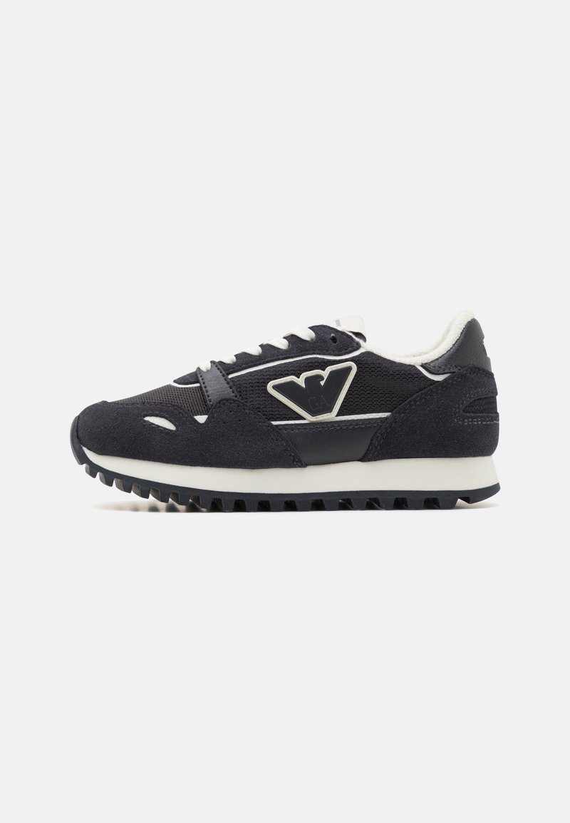 Juodas sportinis batelis su zomšos ir tinklinės medžiagos viršutine dalimi, baltais akcentais, lace-up dizainu ir tekstūruota sole, užtikrinančia sukibimą. Logotipas ant šoninio panelio.