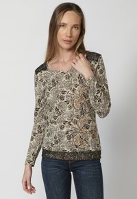 Beige Langarmoberteil mit schwarzen Blumenmustern, ergänzt durch orangefarbene und goldene Akzente. Strukturierte schwarze Spitze als Besatz an den Schultern.