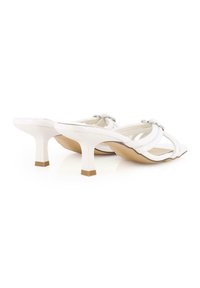 Sandalias de tacón blanco con acabado de cuero suave, que presentan correas entrelazadas y pequeños acentos plateados en la parte superior, con tacones cortos tipo bloque.