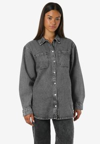 Hallhalli denimmärk, millel on kraega kaelus, nööbid ja kaks esipocketit. Lahtine lõige, pikad varrukad ja sirge äär.