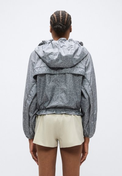 Γκρι μπουφάν με σχέδια, κουκούλα, ελαστική μέση και φαρδιά μανίκια, σε συνδυασμό με ανοιχτόχρωμο σορτς. Έμφαση στο λουλουδένιο μοτίβο και στην υφή.