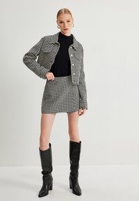 Zwart-witte houndstooth jas- en rokset, gestructureerde stof, cropped ontwerp, gecombineerd met zwarte kniehoge laarzen, zichtbare knopen aan de voorkant.
