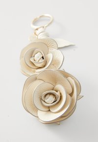 Floral keychain accessory made of textured cream-colored material, featuring layered rose petals and a small center bud, attached to a metal ring.