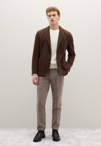 Brauner Blazer mit Kerbkragen, weißer Strickpullover, hellbraune strukturierte Hose und schwarze Schnürschuhe. Nahtloses und modernes Design.