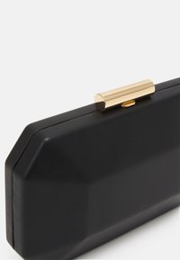 Musta suorakulmainen clutch, jossa on kulmikkaat reunat ja sylinterimäinen kultainen lukko päällä, valkoista taustaa vasten.