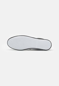Black and white sneaker sole with a textured surface, featuring a white rubber base and a black side trim. Smooth and flat design.