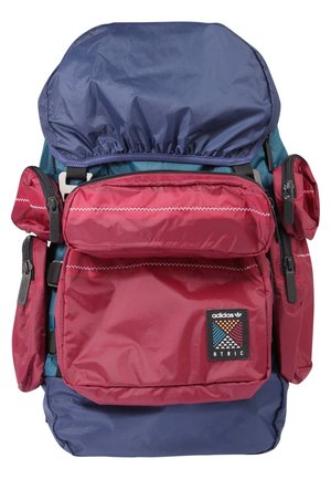 Mehrfarbiger Adidas ATRIC Rucksack mit roten Fronttaschen, blauem Hauptteil, mehreren Reißverschlussfächern und Stoffstruktur.