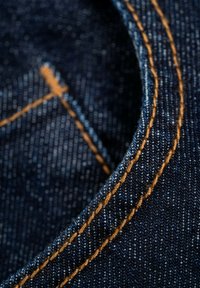 Close-up of dark blue denim fabric with orange double stitching on a curved edge.