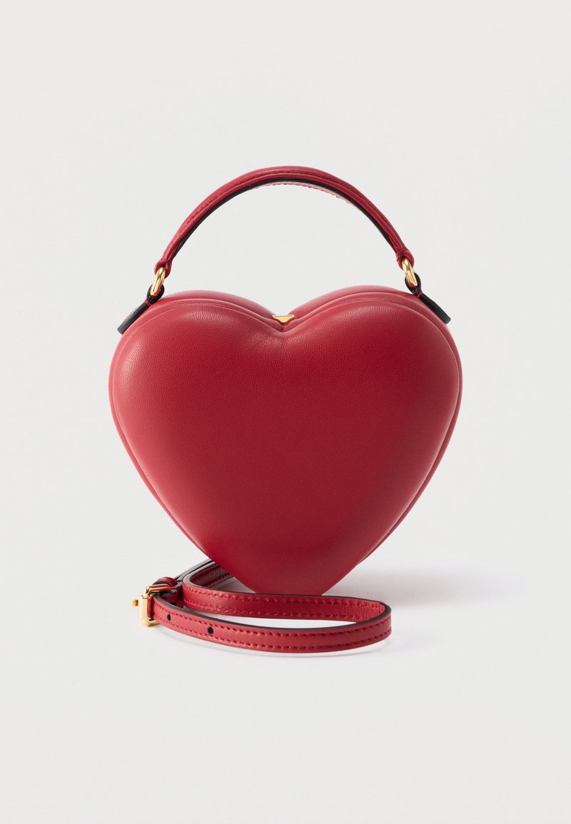 Sac à main en cuir rouge en forme de cœur avec une poignée supérieure et une bandoulière détachable sur un fond uni.