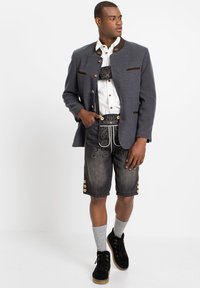 Giacca tradizionale grigio scuro con accenti marroni, camicia bianca, pantaloni corti scuri ricamati, calze grigie fino al ginocchio e scarpe nere.