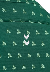 Ciemnozielona tkanina z kontrastowymi jasn Zielonymi wzorami kwiatowymi oraz białymi akcentami w zygzak. Gładka faktura, wyraźnie zarysowane szwy.