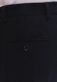 Granatowe spodnie o gładkiej fakturze, z płaskim przodem i jedną tylną kieszenią zapinaną na guzik.