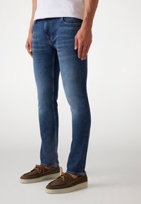 Donkerblauwe skinny jeans met een gladde textuur, vijf-pocket ontwerp en lichte vervaging. Gecombineerd met bruine veterschoenen met een lichte zool.